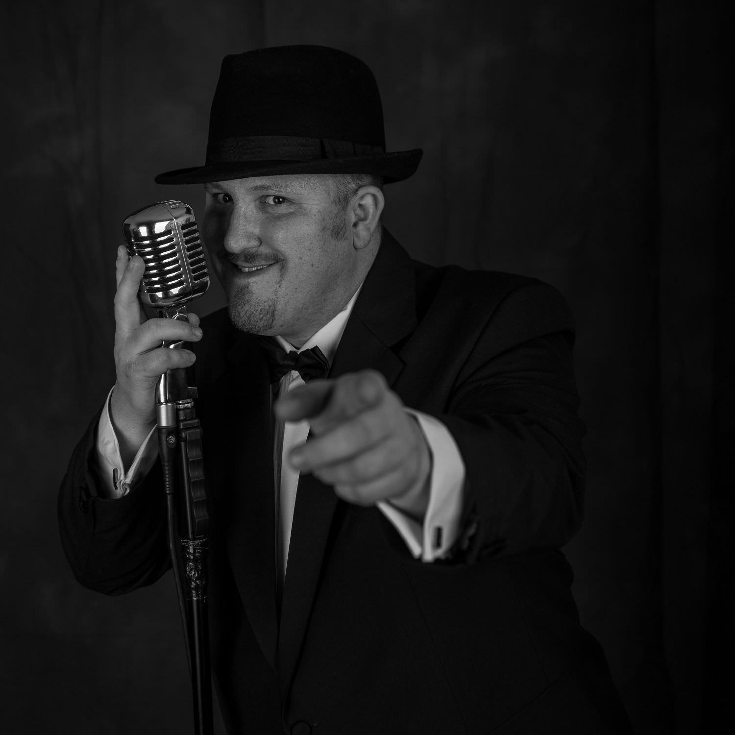Jon paul swing singer points at camera while caressing back of vintage microphone on stand.