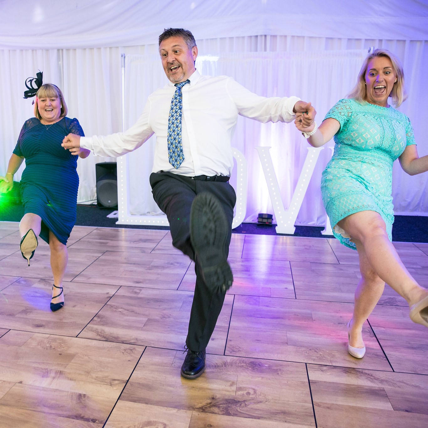 Man holding hands with two women on dance floor as they dance can-can at south wales wedding.