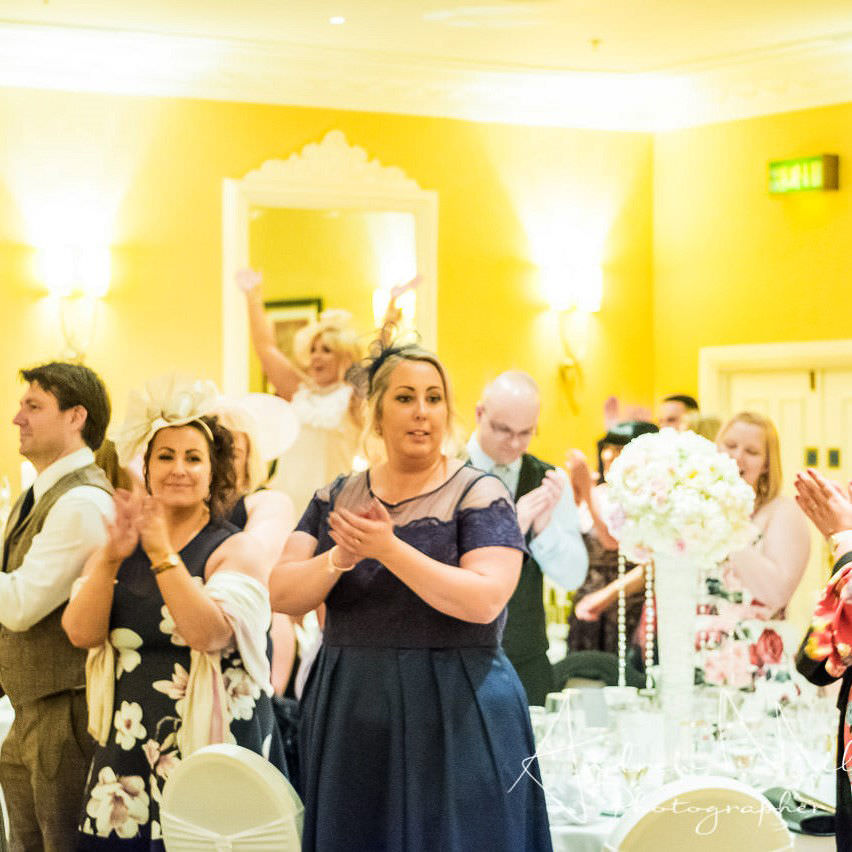 Guests stand dancing and clapping at tables during daytime singing waiter show in south wales.