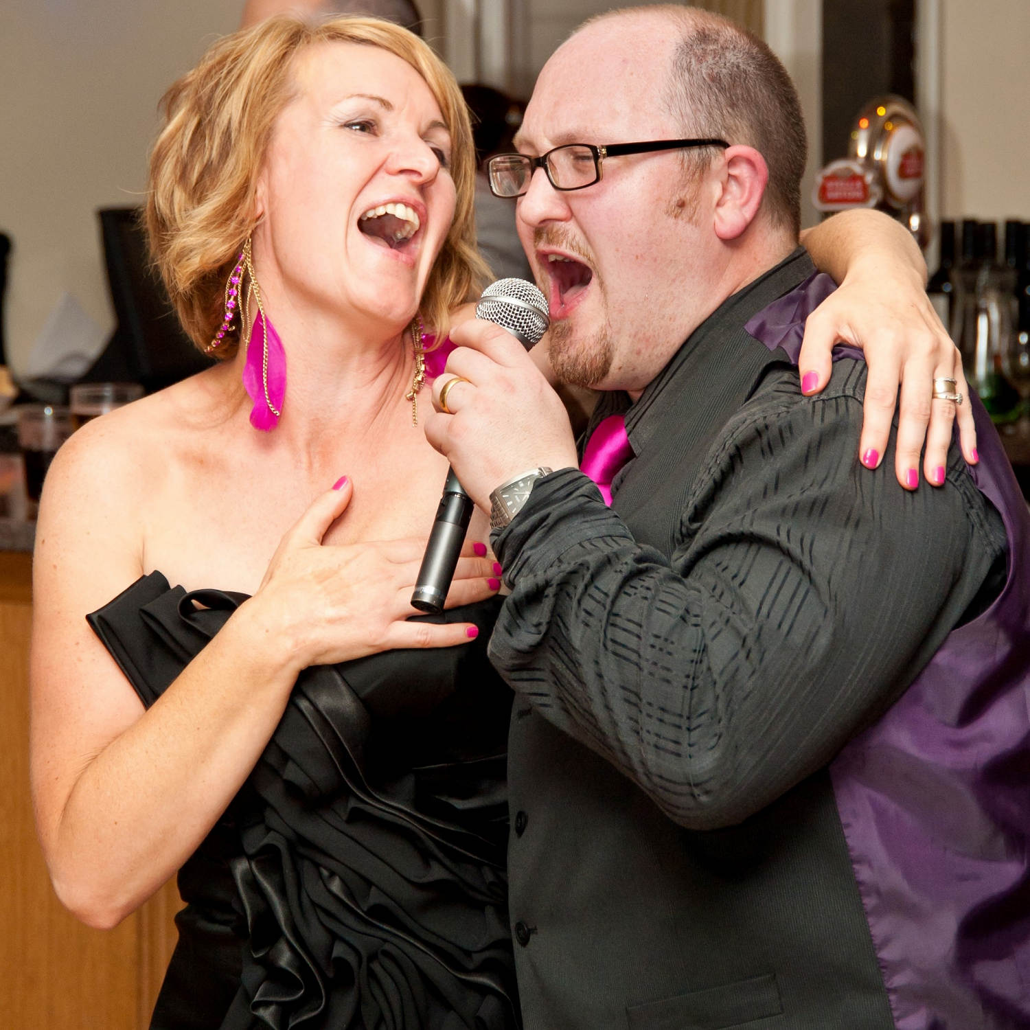 A female party guest sings along with her arm draped over shoulders of Jon Paul singer at wedding reception in wales.