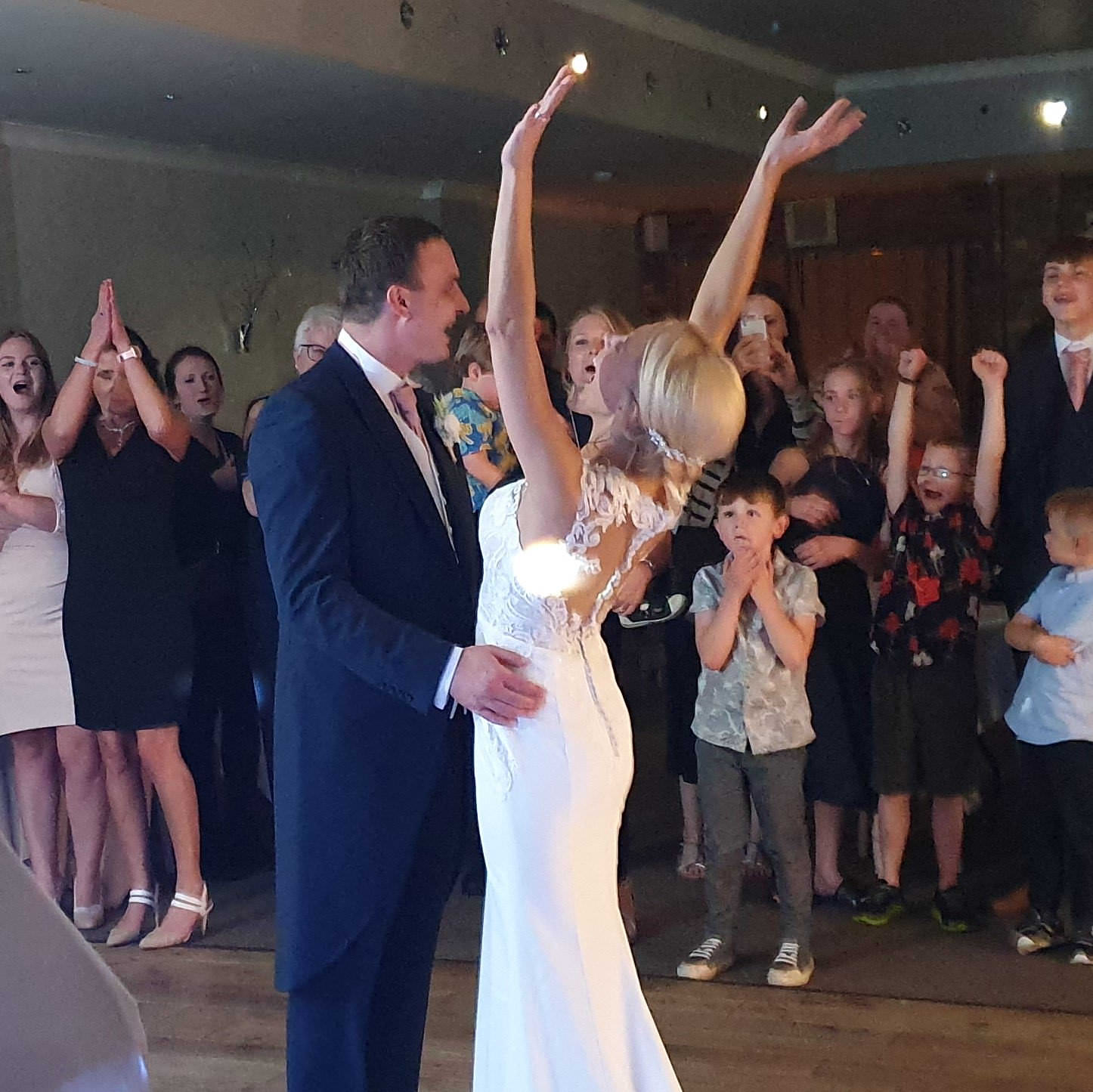 Bride and groom with her arms victoriously punching air above head during first dance at wedding disco near Bristol.