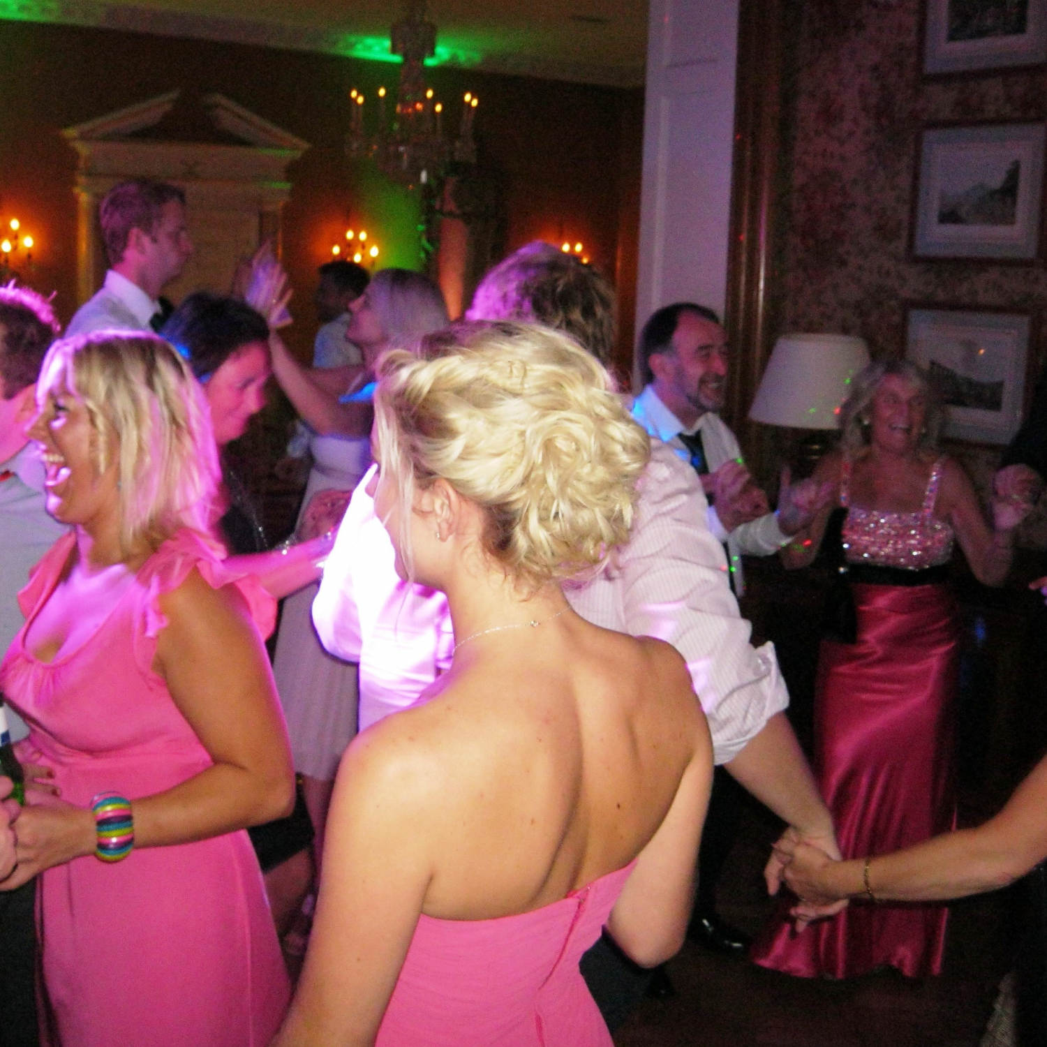 Family hold hands while bridesmaids in pink gowns laugh at wedding disco in Georgian era building near bristol.