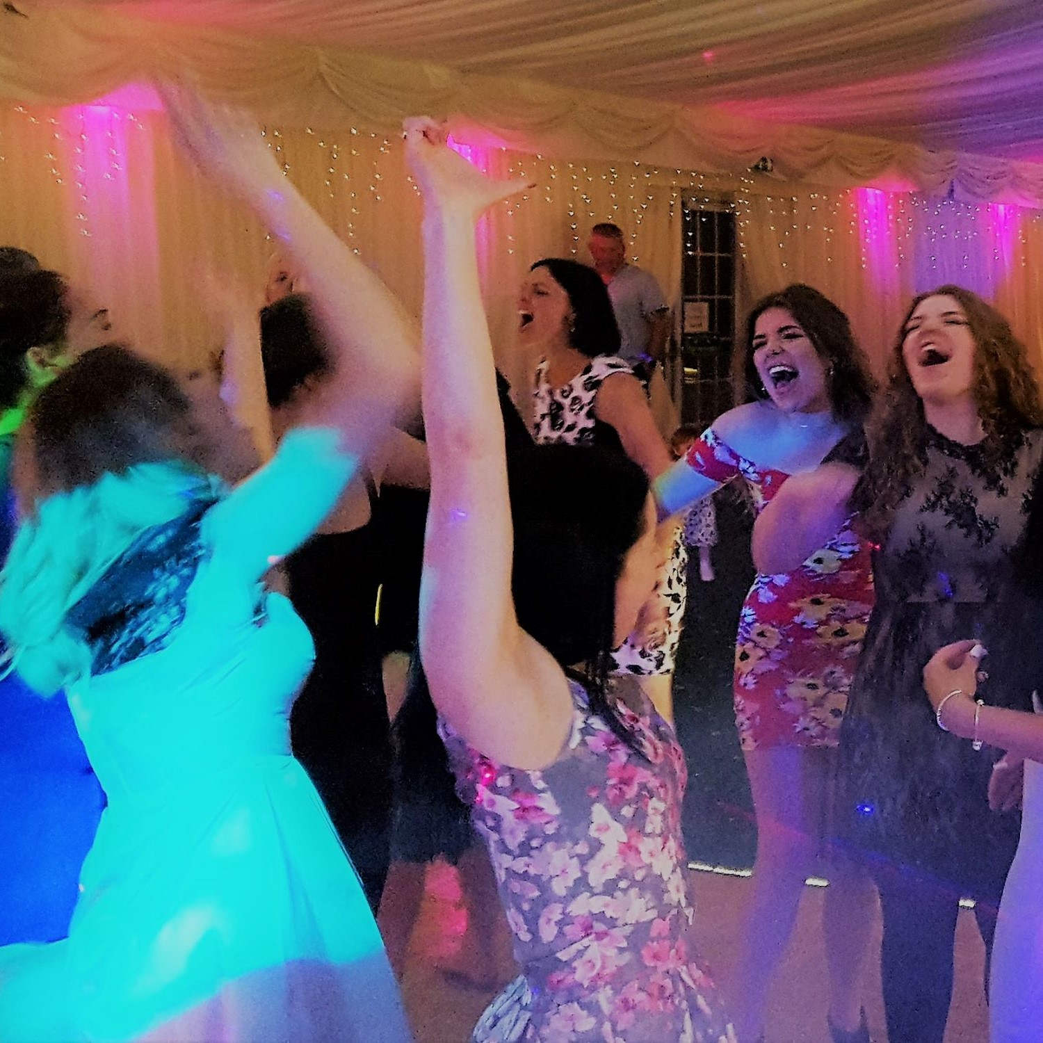 Laughing and dancing group of young women punch the air and sing along at wedding party near bristol.
