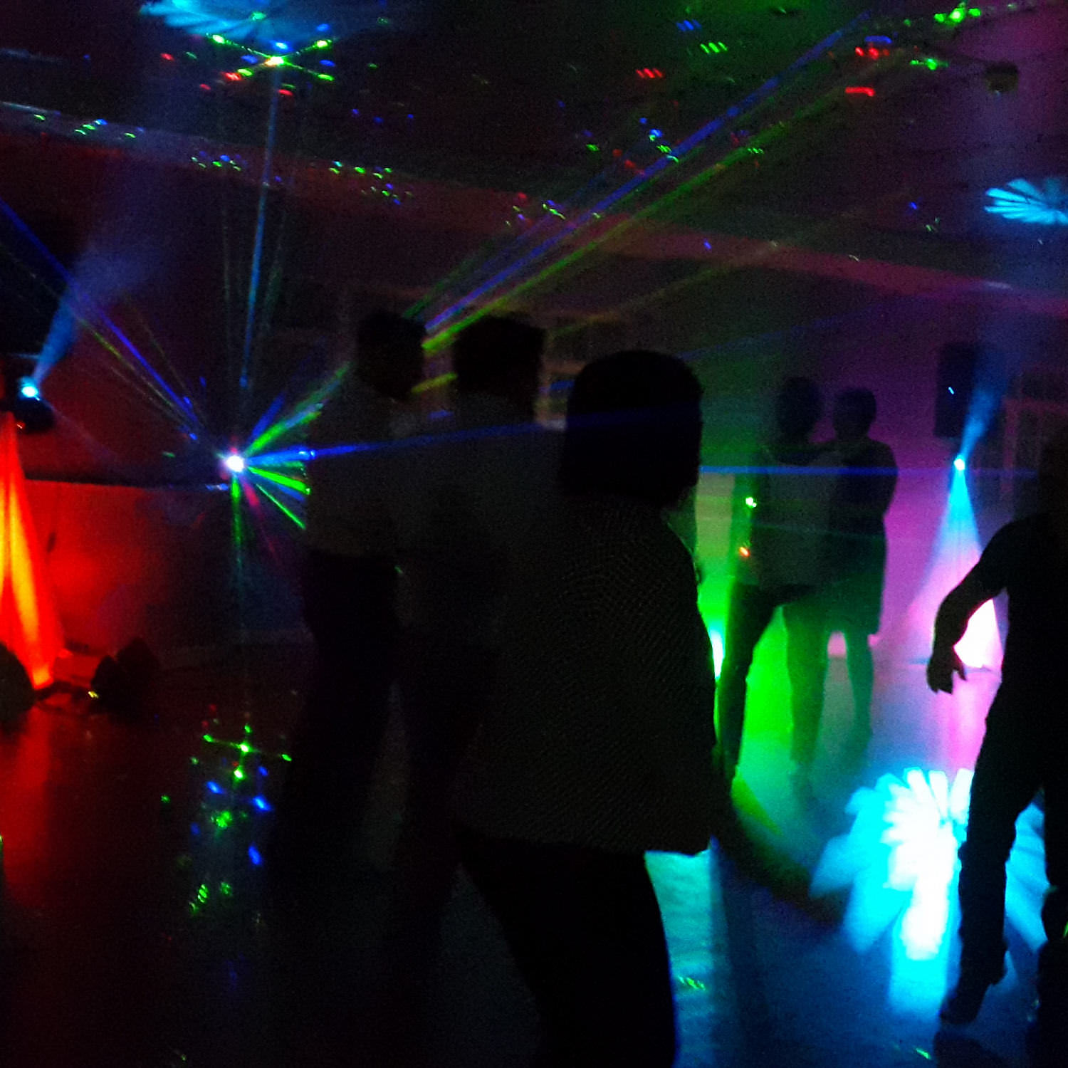 Party dancers in silhouette and multicolour lights and laser beams hang in the air.