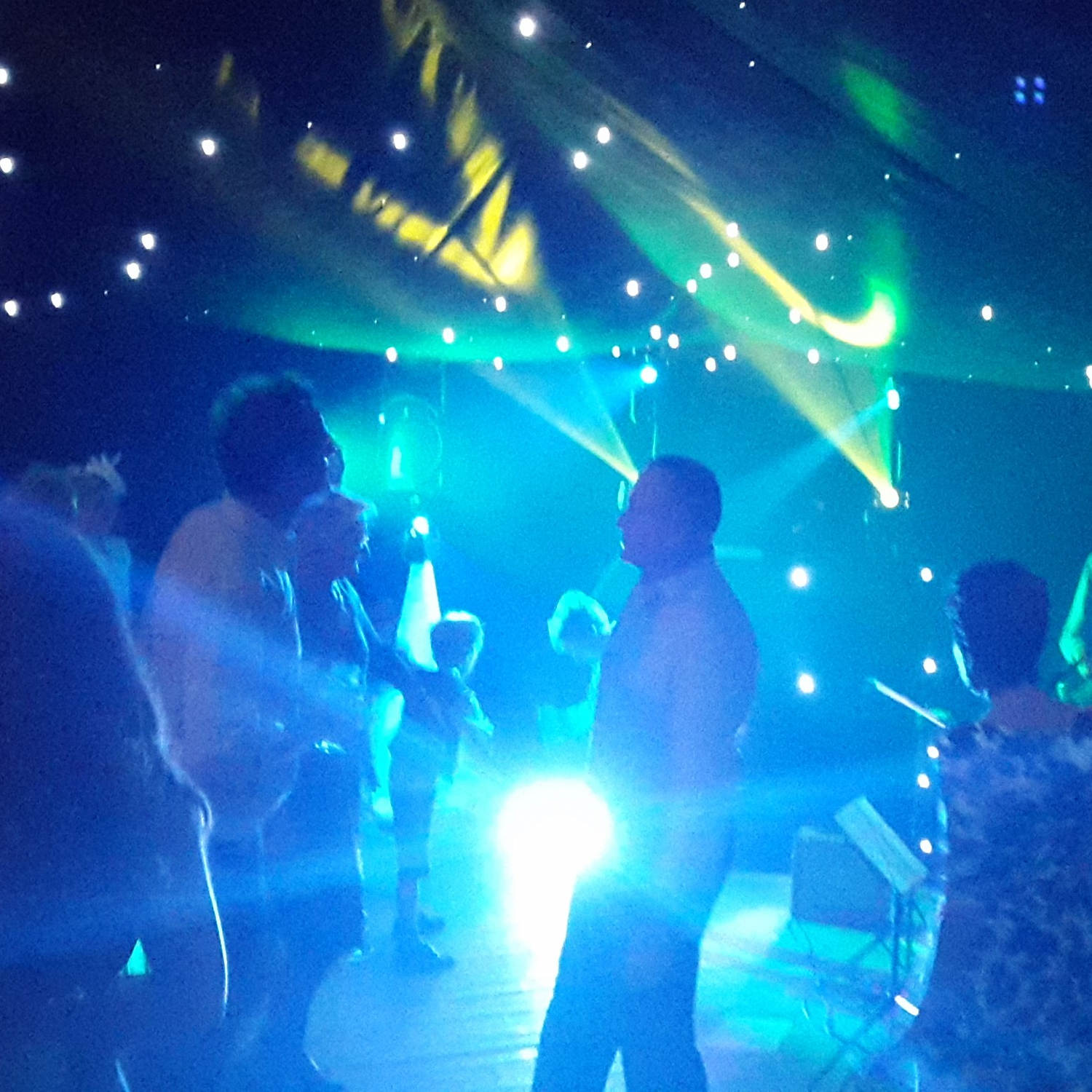 Wedding party dancers lit in blue with searchlights and sparkling starcloth behind them.