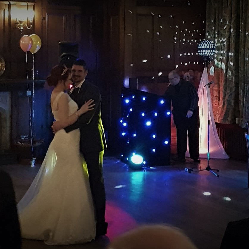 Bride and groom embrace and smile off camera while jon paul wedding singer performs in background near bristol.